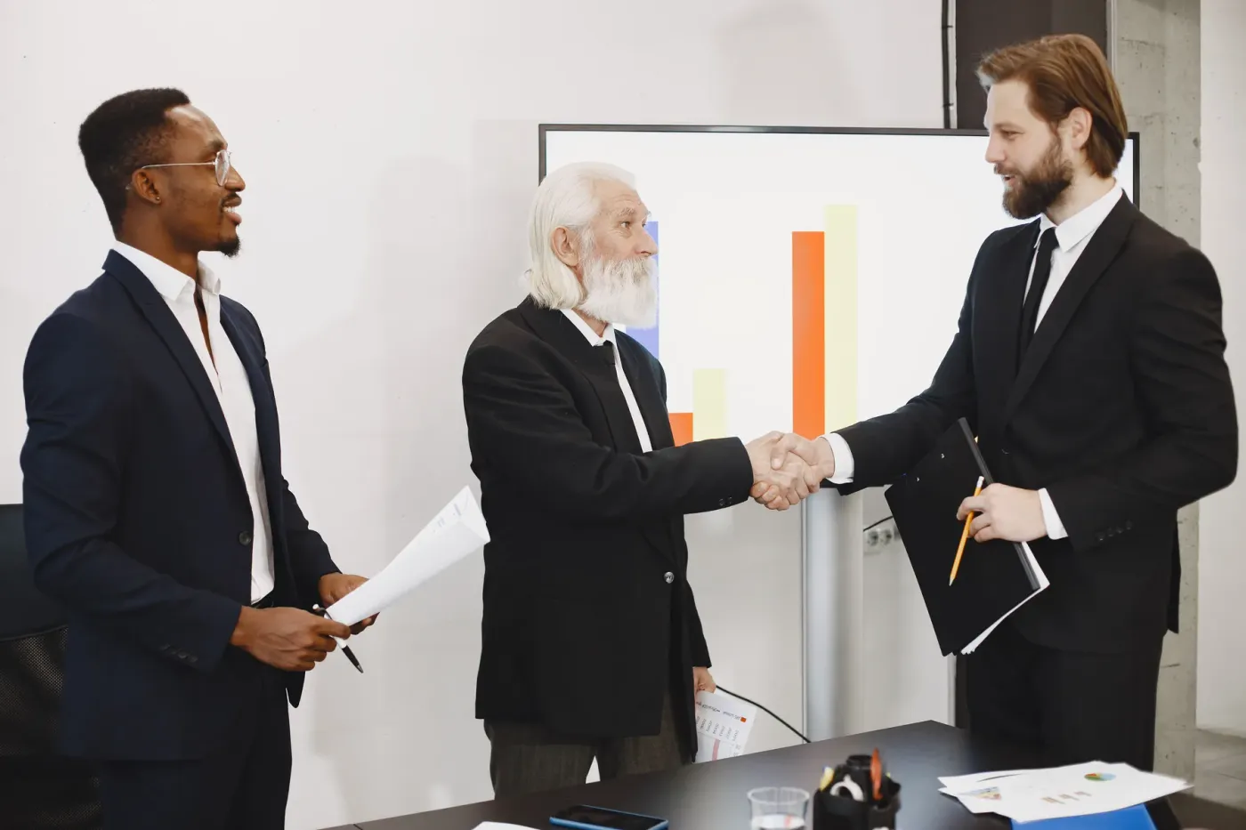 Two professionals shaking hands after a meeting, with a colleague looking on