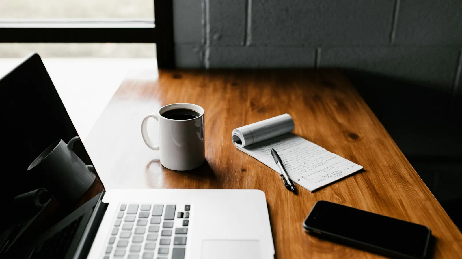 A laptop, a white mug and a smartphone on a light desk